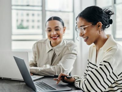Business women, laptop and and happy team in office  for web design, collaboration and training. Planning, digital marketing and coaching by woman leader menor help, explain and support creative goal